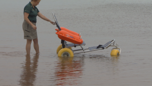 wheelchair in water it has floatation devices as arm rests and a metal frame like a shopping cart.